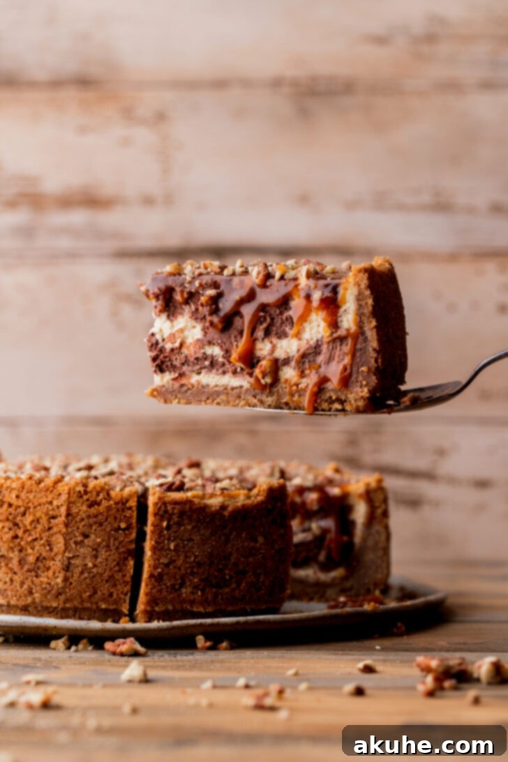 A perfectly sliced piece of Turtle Cheesecake being taken out, revealing the creamy layers, crunchy crust, and rich caramel topping.