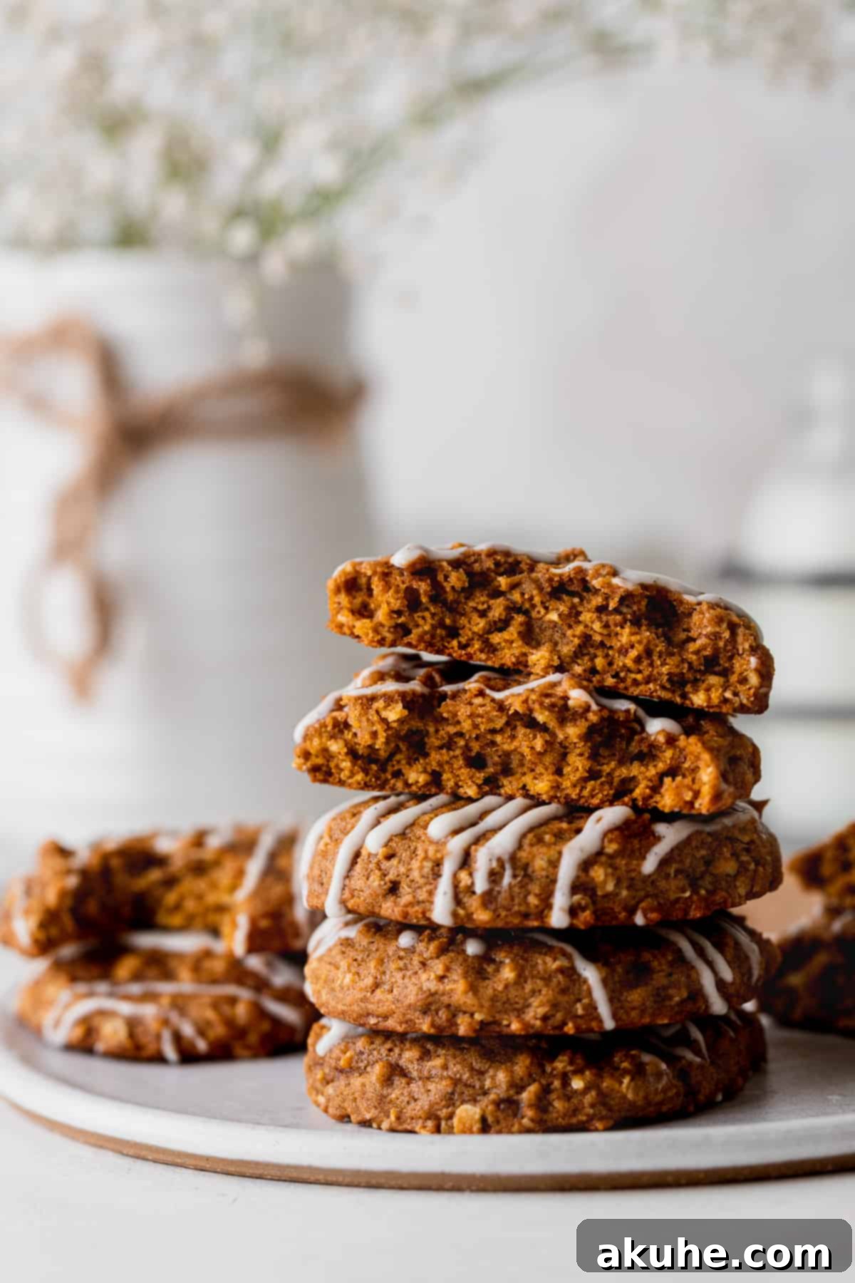A stack of golden-brown pumpkin oatmeal cookies, each beautifully drizzled with cream cheese glaze.