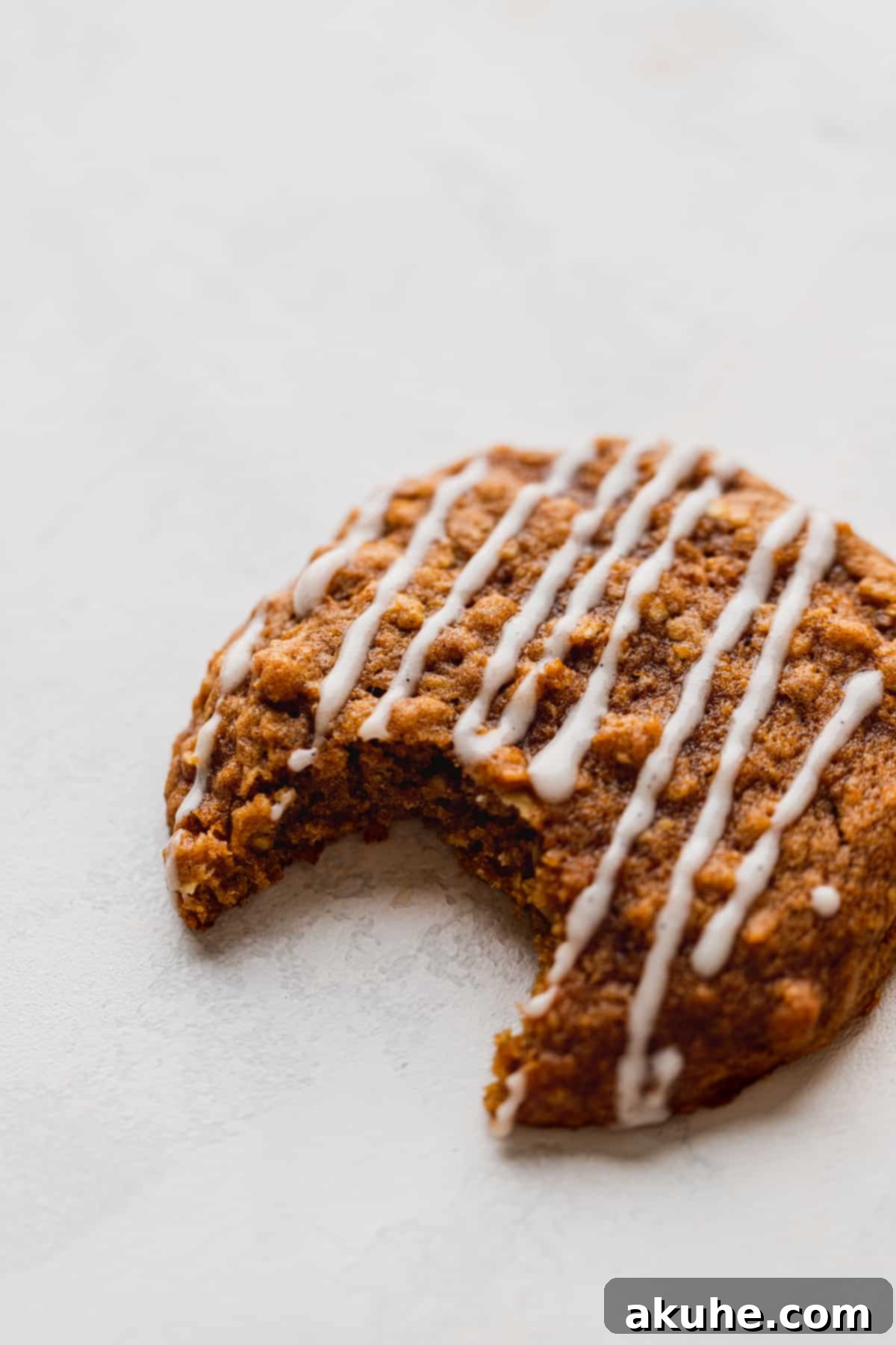 A close-up shot of a pumpkin oatmeal cookie with a bite taken, highlighting the creamy glaze.
