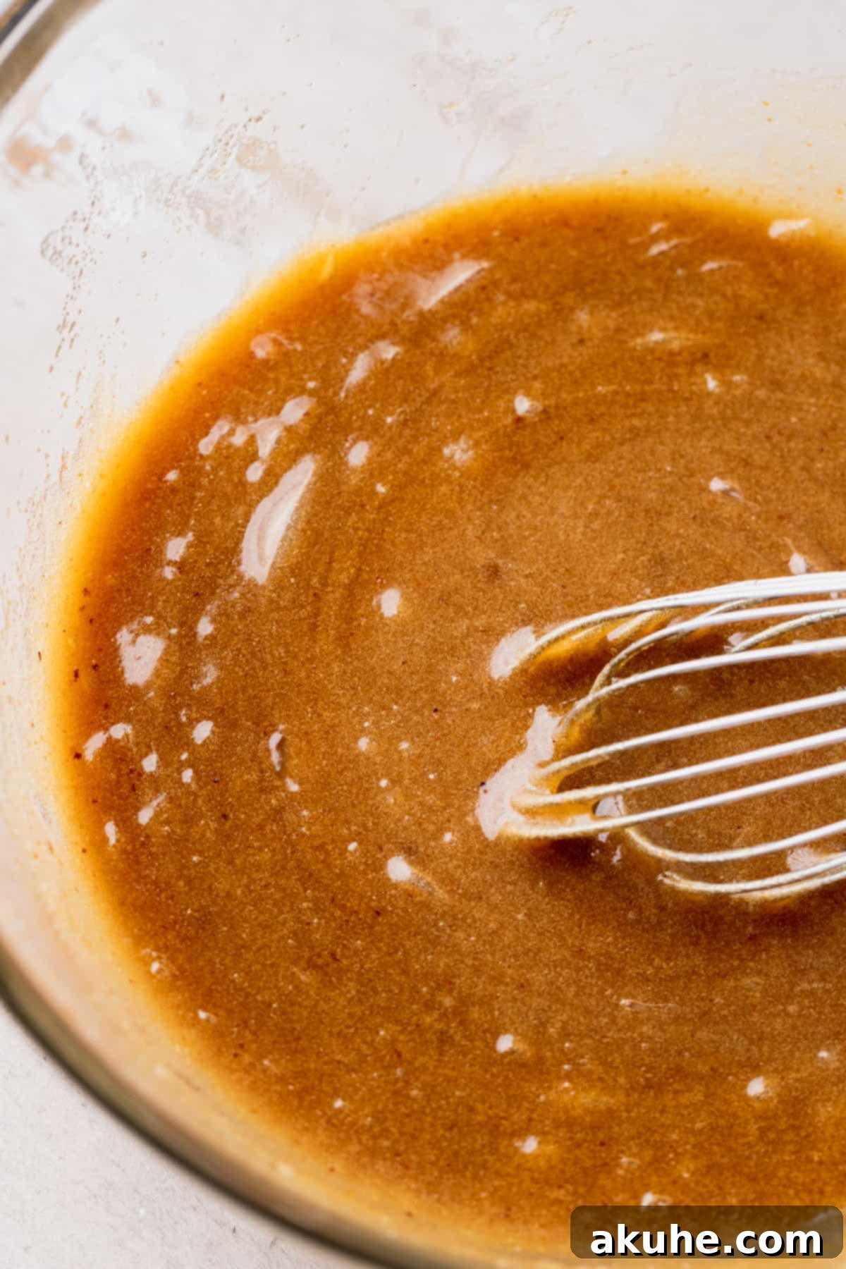 A bowl of mixed wet ingredients, including brown butter, sugars, and eggs, looking smooth and creamy.