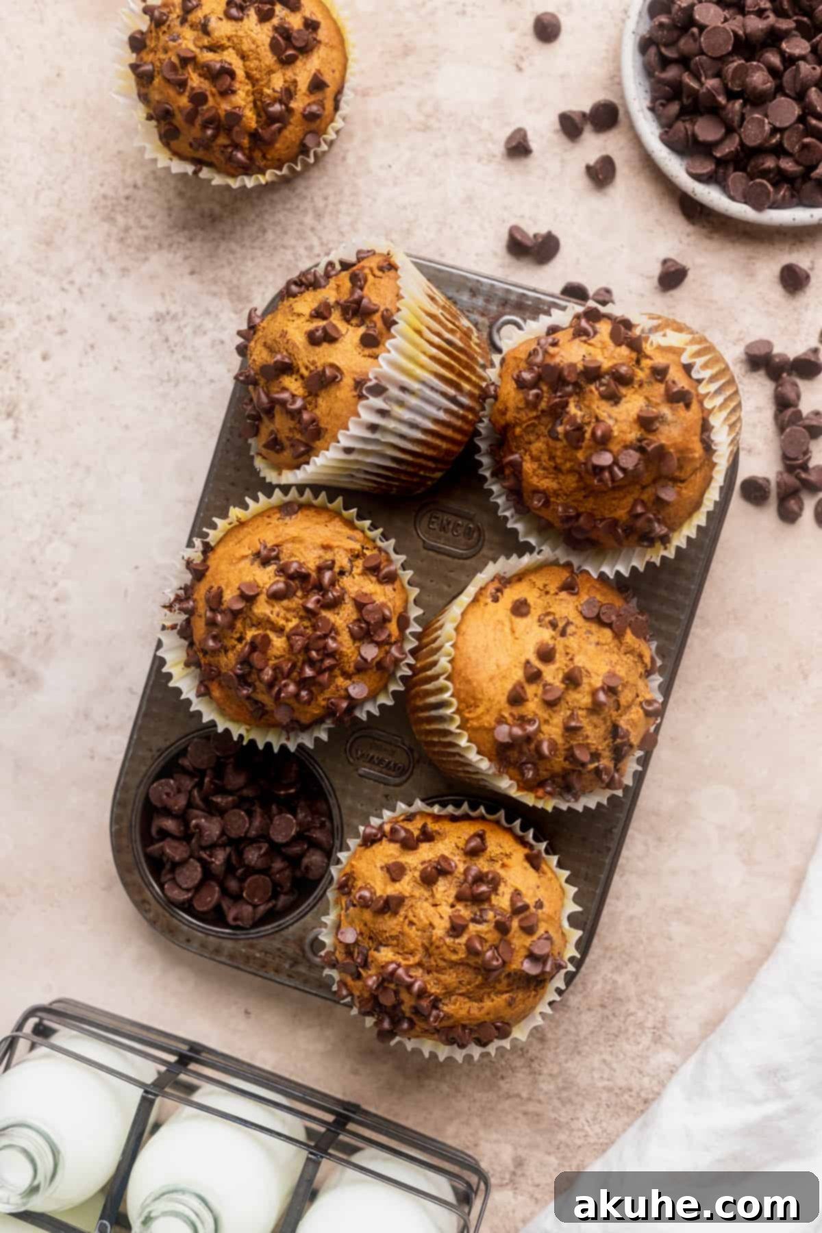 A freshly baked tray of golden brown pumpkin chocolate chip muffins, still warm from the oven.