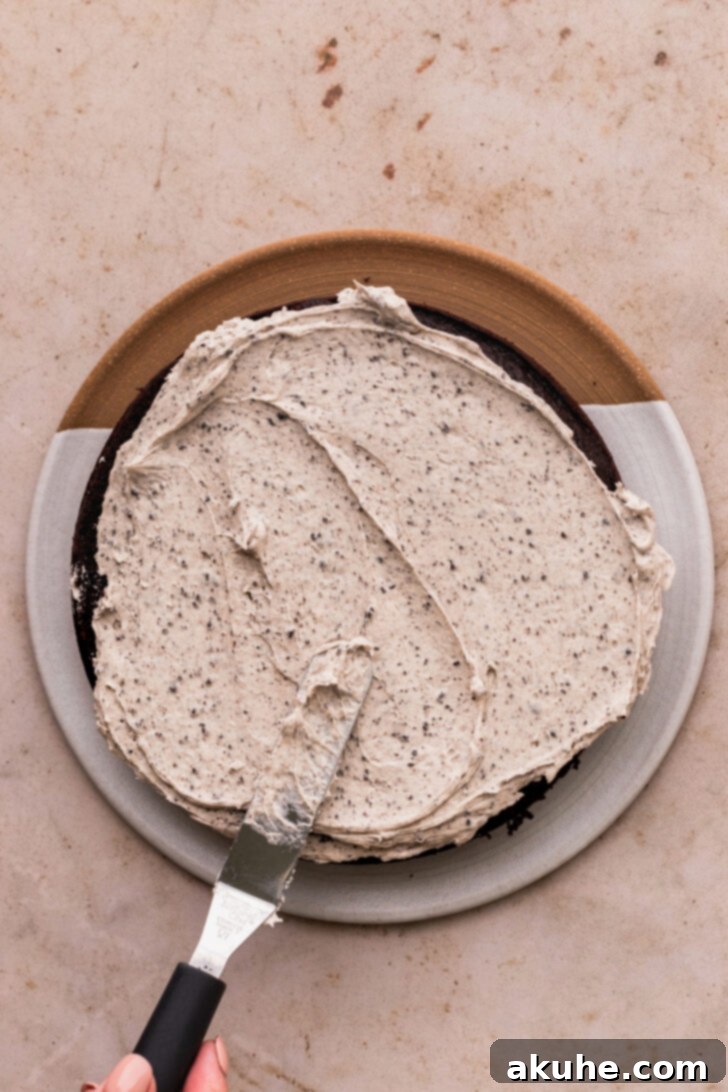 Decadent Oreo Dream Cake 8 Spreading Oreo cream cheese frosting evenly on a chocolate cake layer