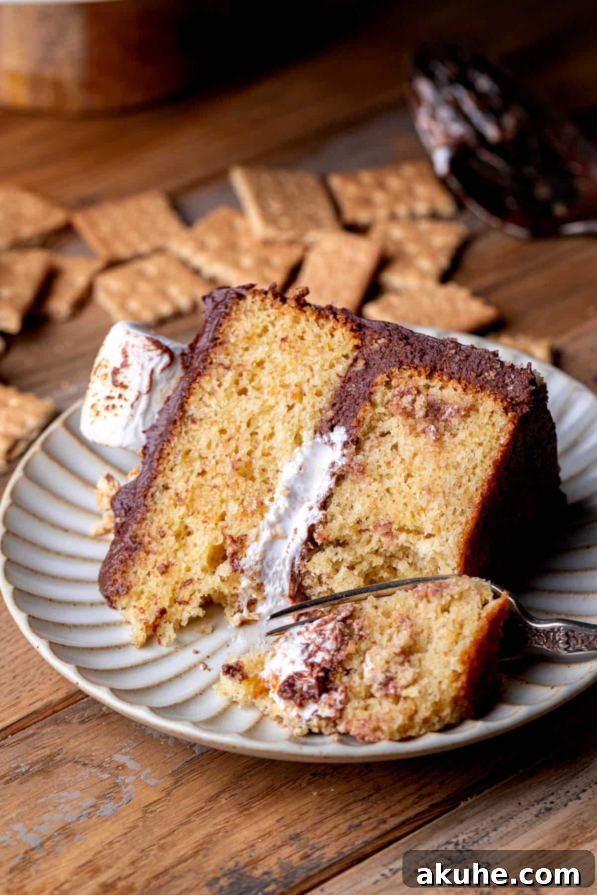 Ultimate Smores Cake 12 Slice of s'mores cake on a plate with a bite missing, showcasing its deliciousness.