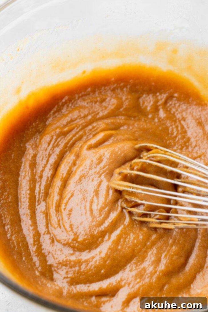 Kitchen Sink Cookies 4 Wet ingredients in a bowl, including melted butter, sugars, peanut butter, eggs, and vanilla, being whisked together.