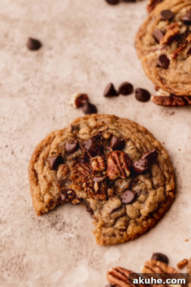 Toasted Pecan Chocolate Chip Delights 9 A close-up of a pecan chocolate chip cookie with a bite taken out, revealing its soft, chewy interior.
