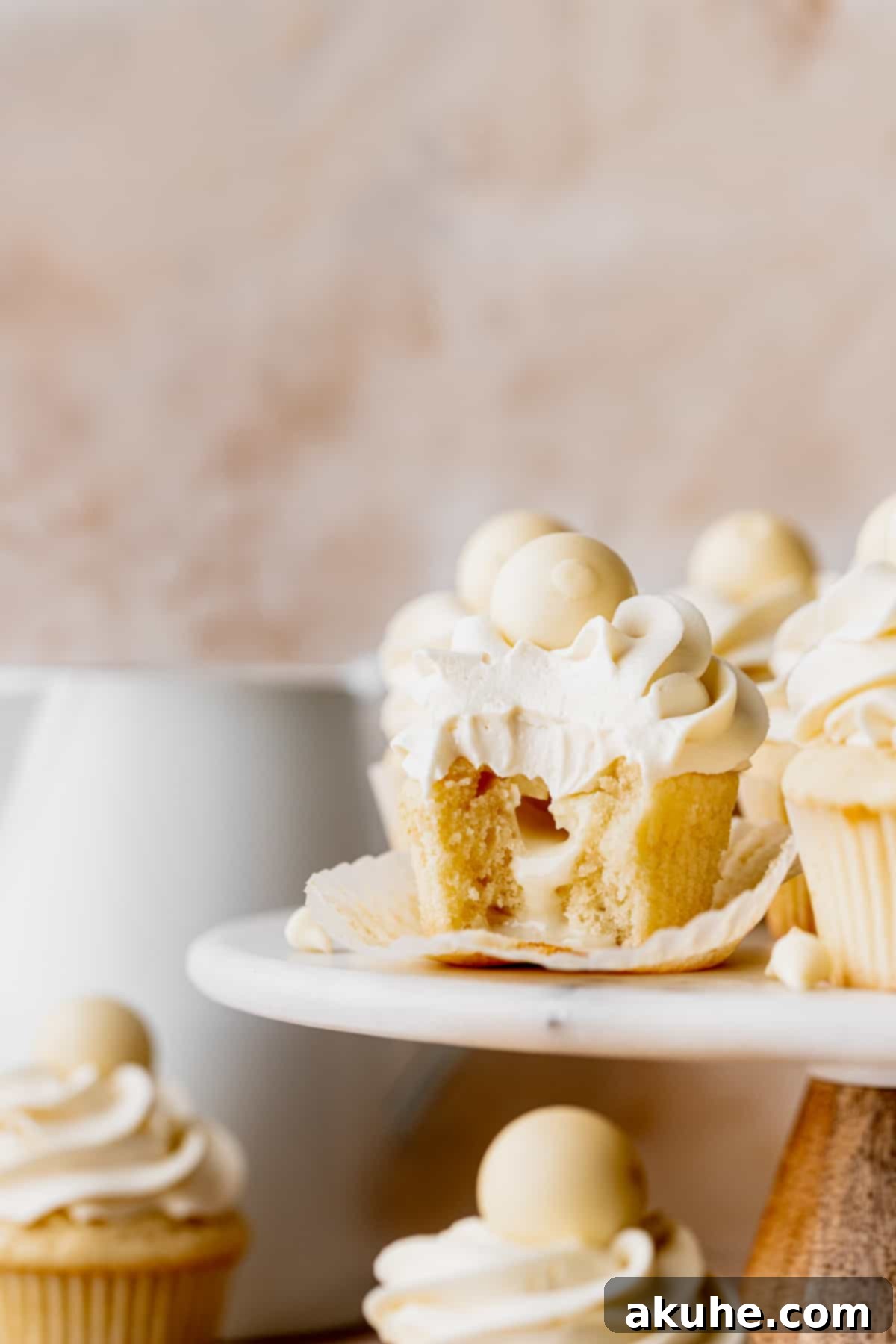 Decadent White Chocolate Cupcakes 2 A delectable white chocolate truffle cupcake with a bite taken out, revealing its creamy truffle core, placed elegantly on a cake stand.