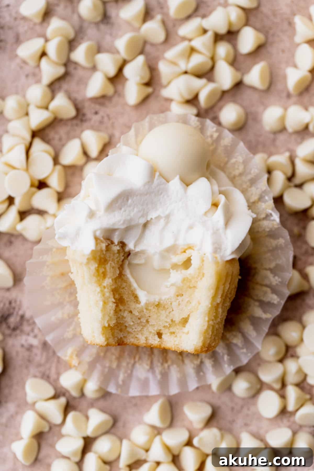 Decadent White Chocolate Cupcakes 10 A charming white chocolate truffle cupcake with a bite removed, surrounded by a scattering of white chocolate chips, highlighting its luscious interior.