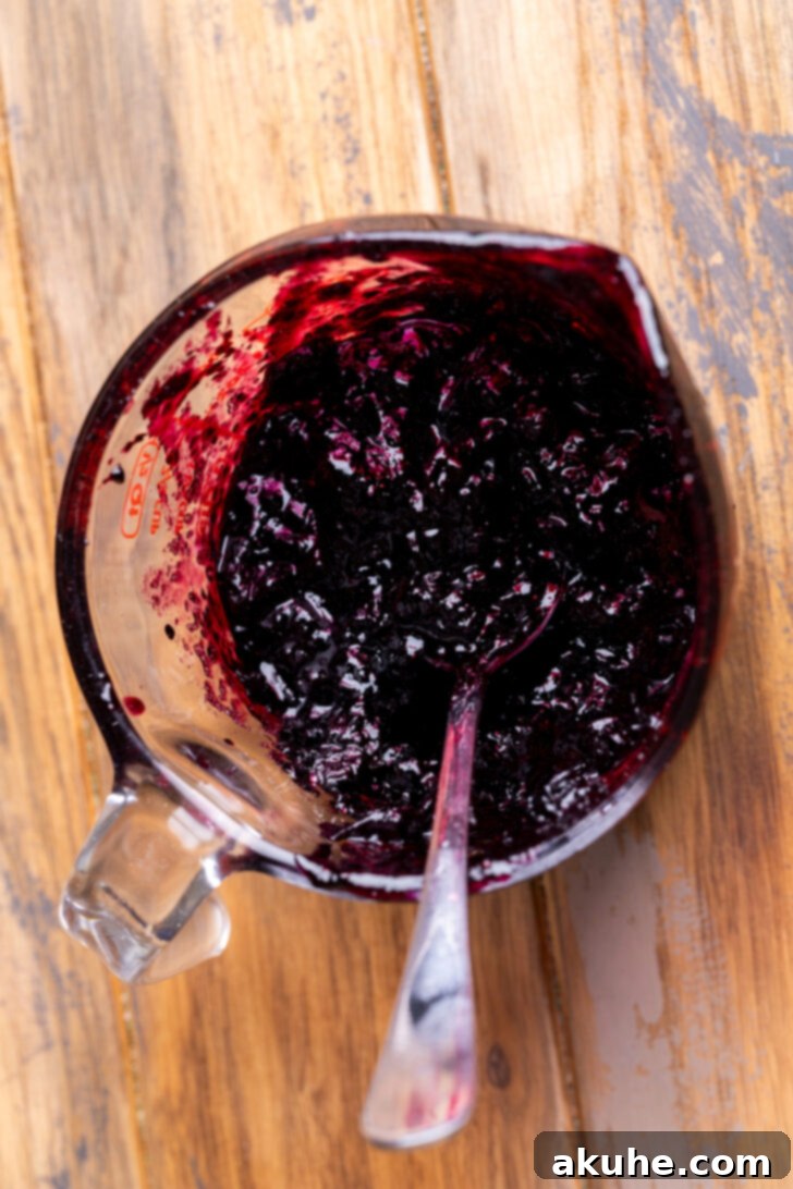 Blueberry Bliss Cake 8 Thick, glossy homemade blueberry jam in a glass measuring cup, ready for spreading after cooling.