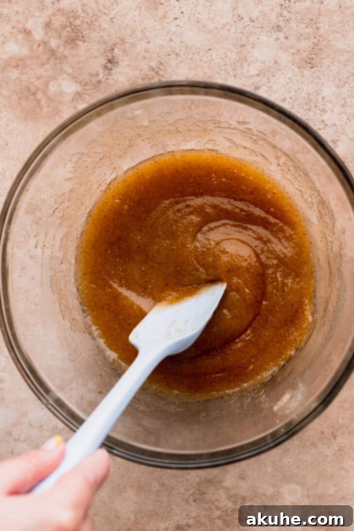 A bowl of wet ingredients, including brown butter, sugar, eggs, and vanilla, being mixed with a whisk.