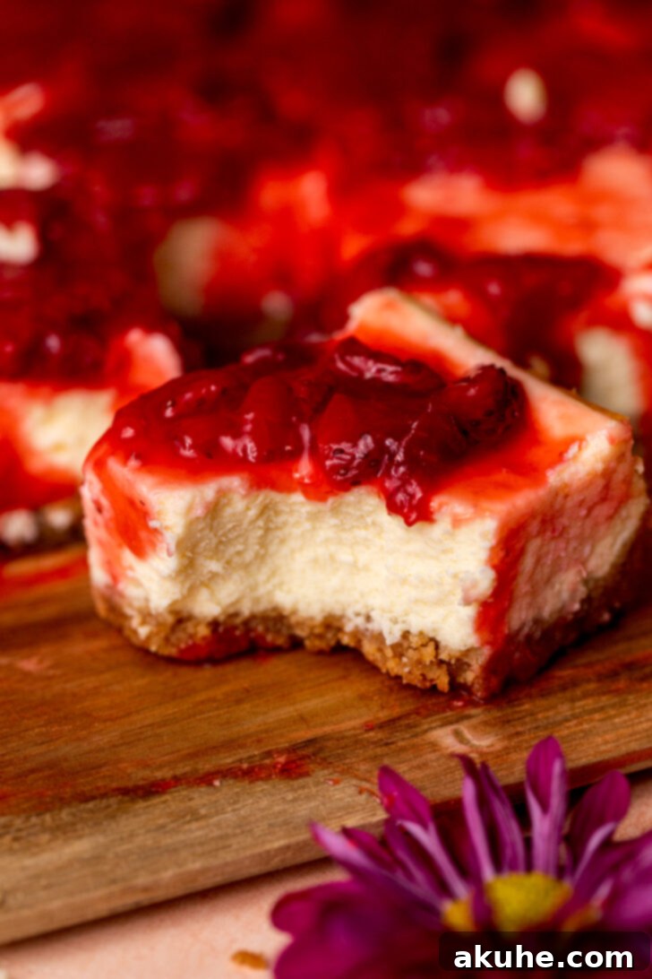 Strawberry Cheesecake Squares 2 A delectable strawberry cheesecake bar with a bite taken, showcasing its layers.