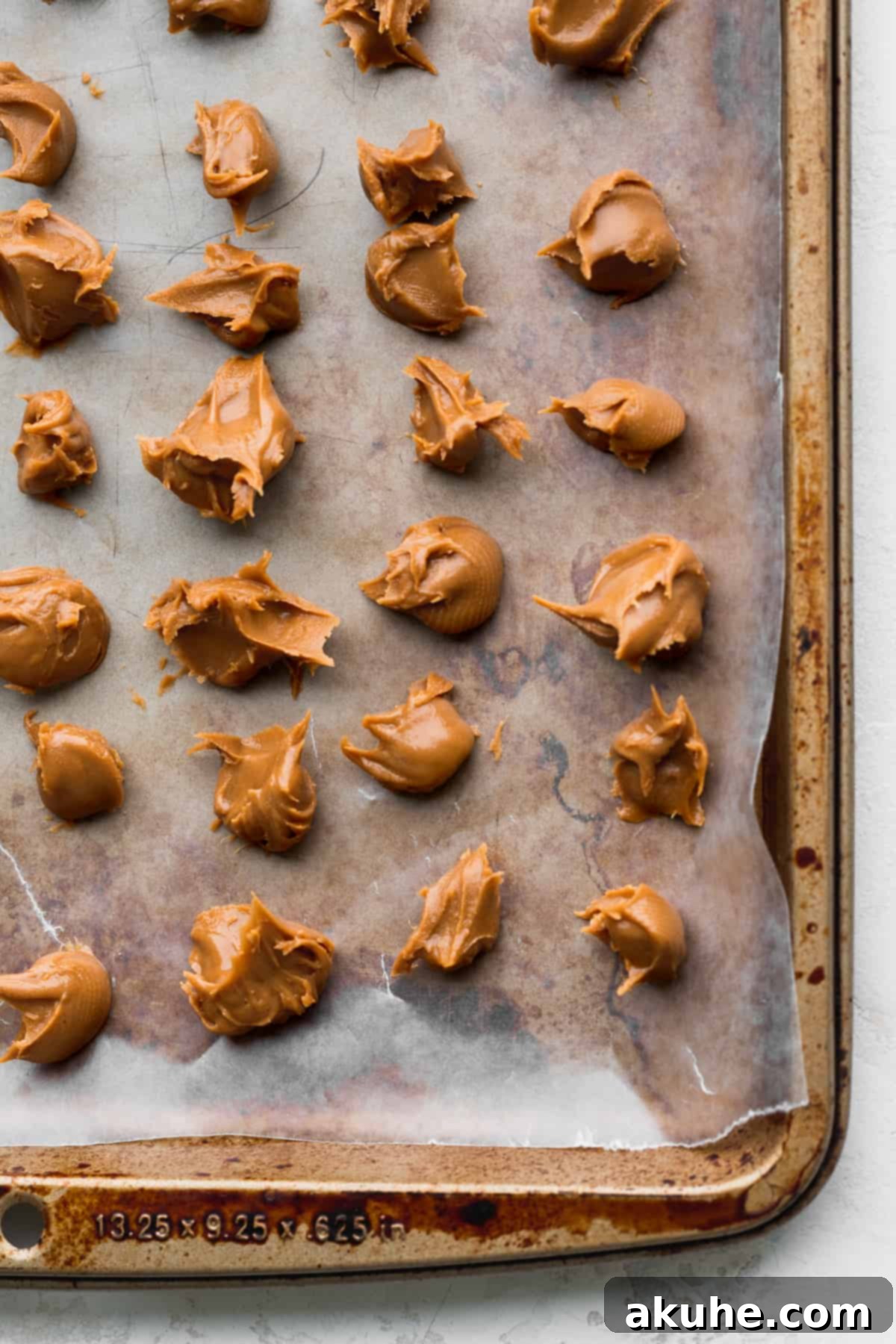 Small, frozen dollops of Biscoff cookie butter artfully arranged on a parchment-lined cookie sheet, ready for topping.