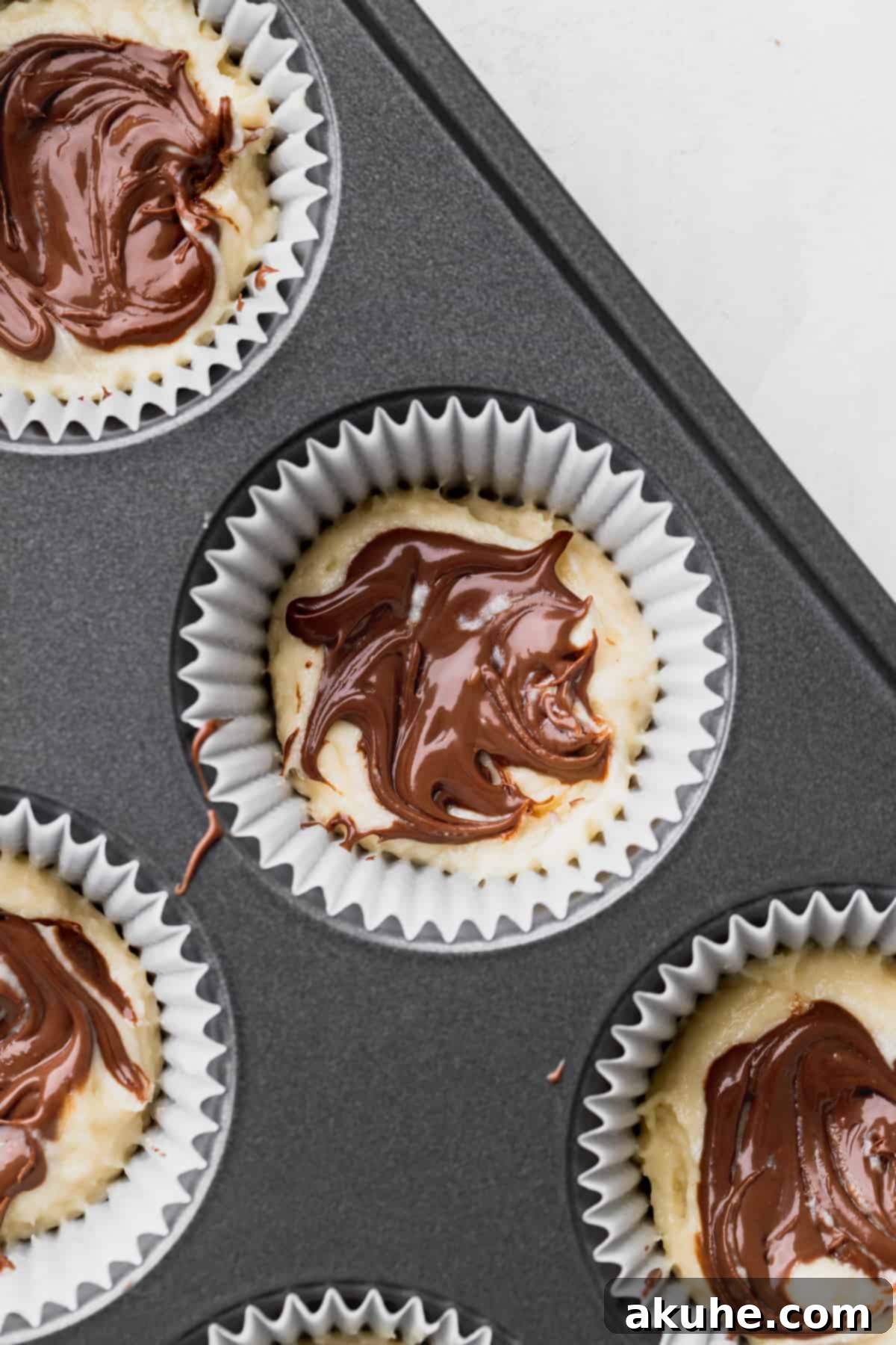 Irresistible Vanilla Nutella Cupcakes 5 A small spoonful of Nutella being delicately swirled into the first layer of vanilla cupcake batter in a lined muffin tin.