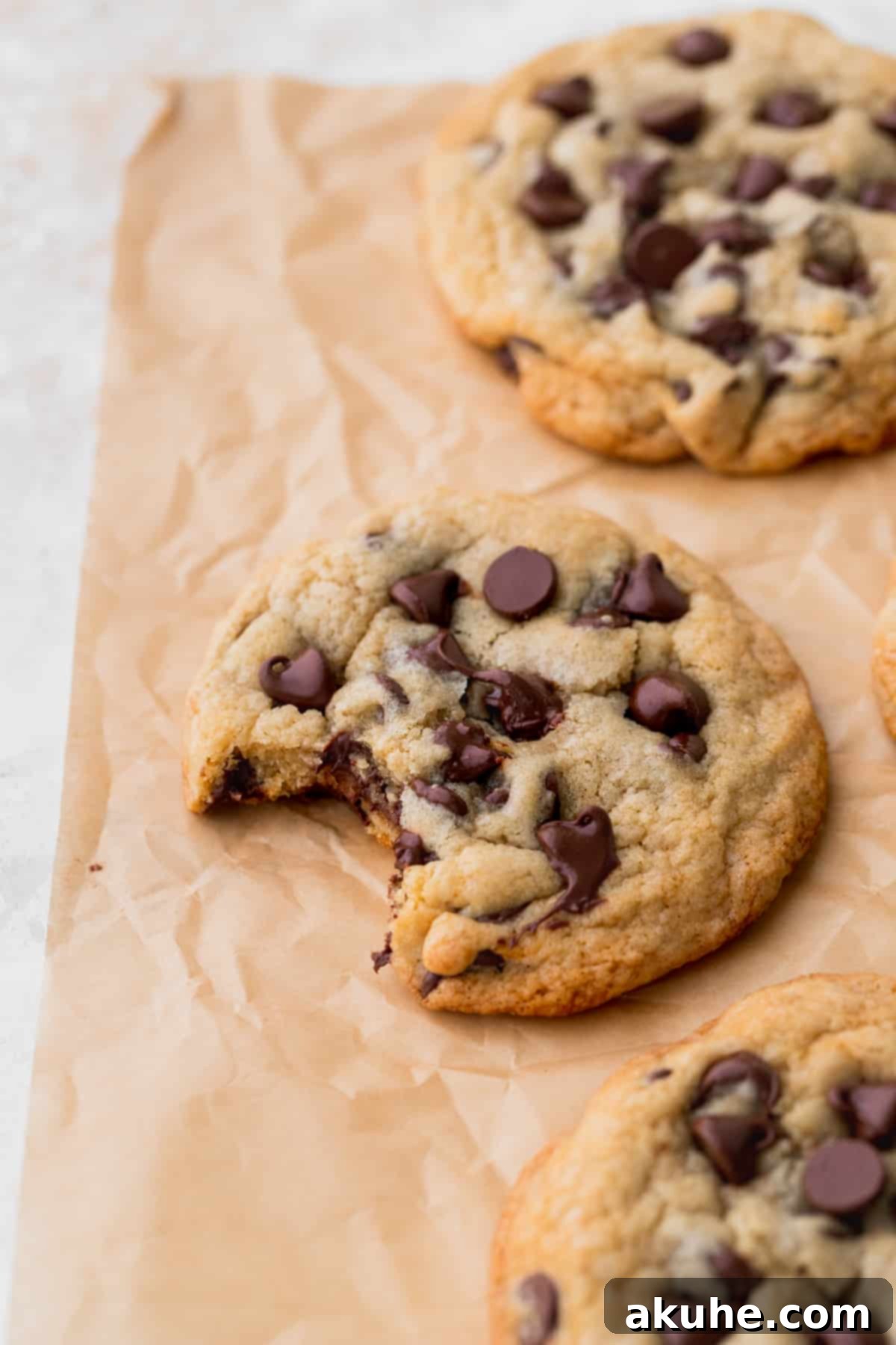 Just Enough Chocolate Chip Bliss 3 A small batch chocolate chip cookie with a bite taken out, resting on parchment paper, revealing its soft and gooey interior.