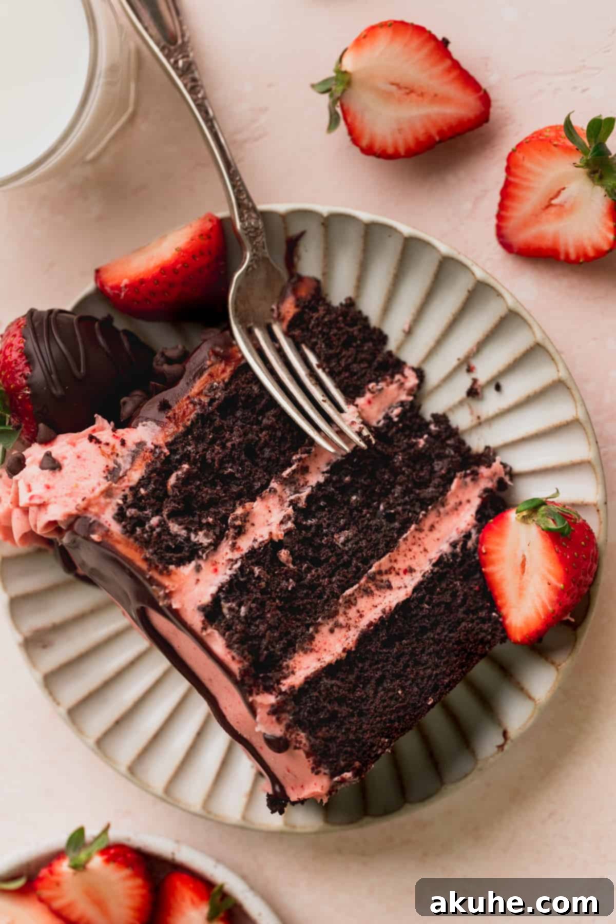 A delectable slice of chocolate covered strawberry cake on a white plate with a fork, ready to be enjoyed.