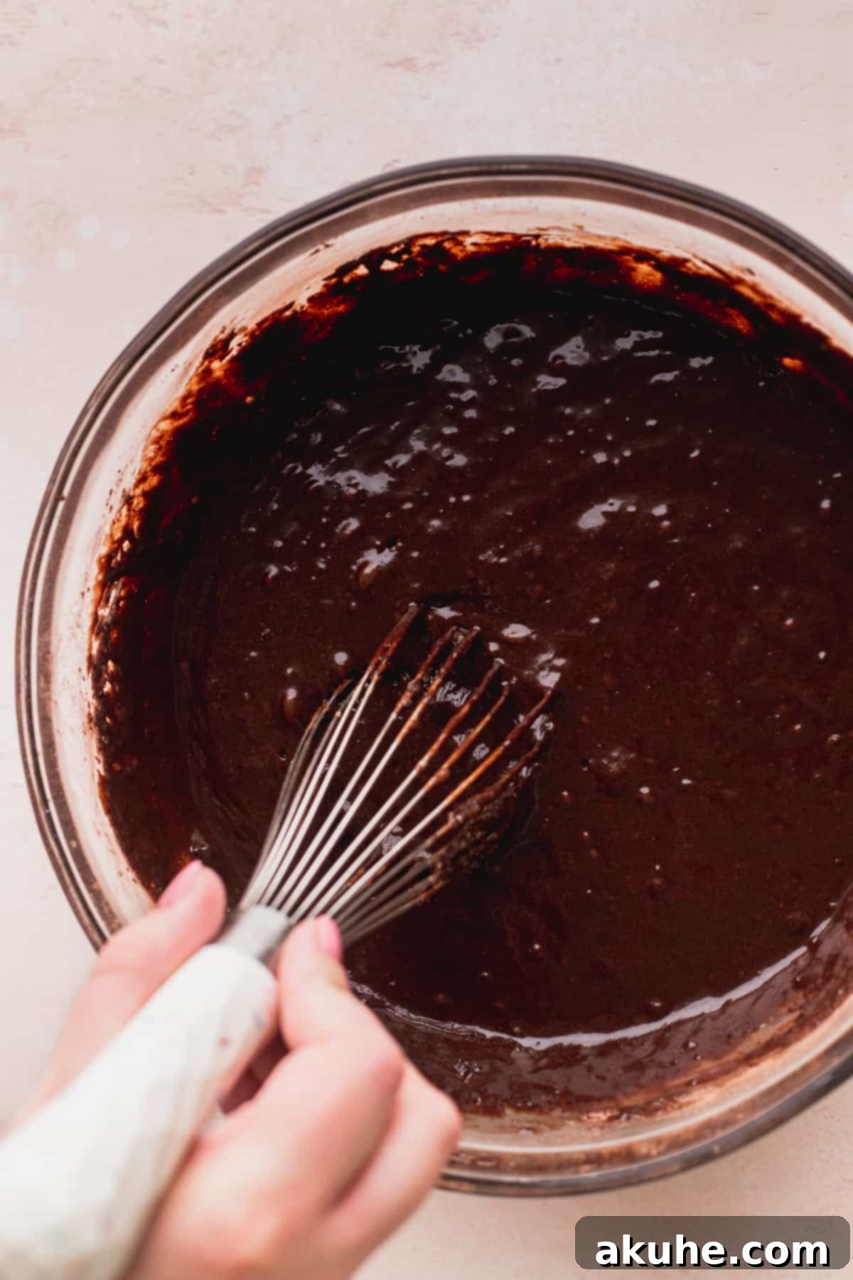 Combining wet and dry ingredients to form the rich chocolate cake batter in a glass bowl.