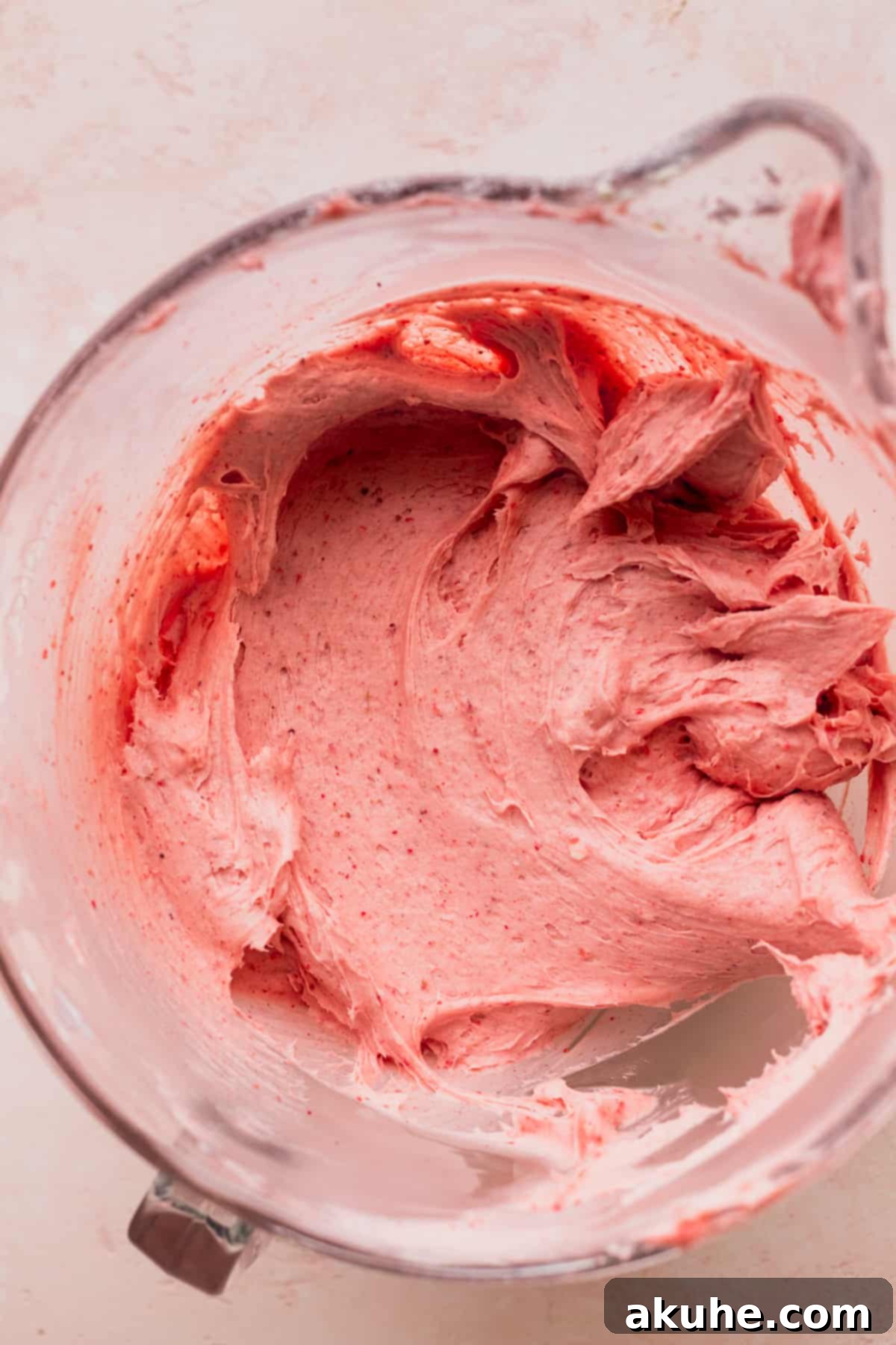 Light pink strawberry cream cheese frosting in a glass mixing bowl, perfectly smooth and ready for use.
