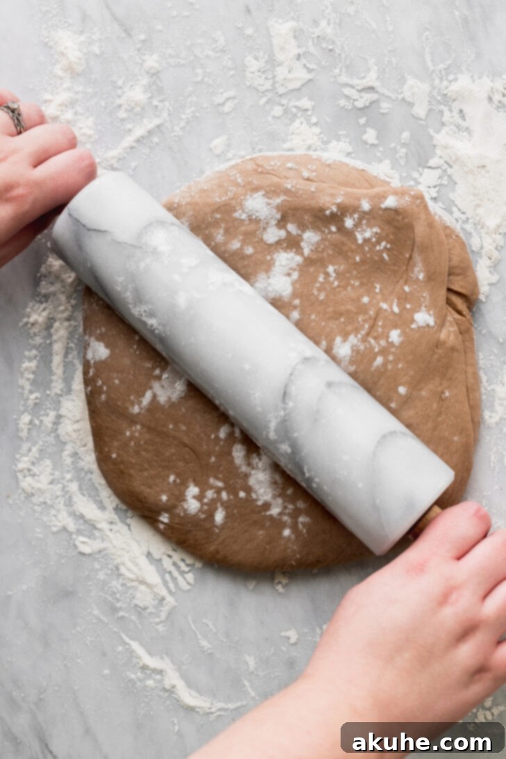 Dough being rolled out on a floured surface to an even rectangle, showcasing its elasticity.