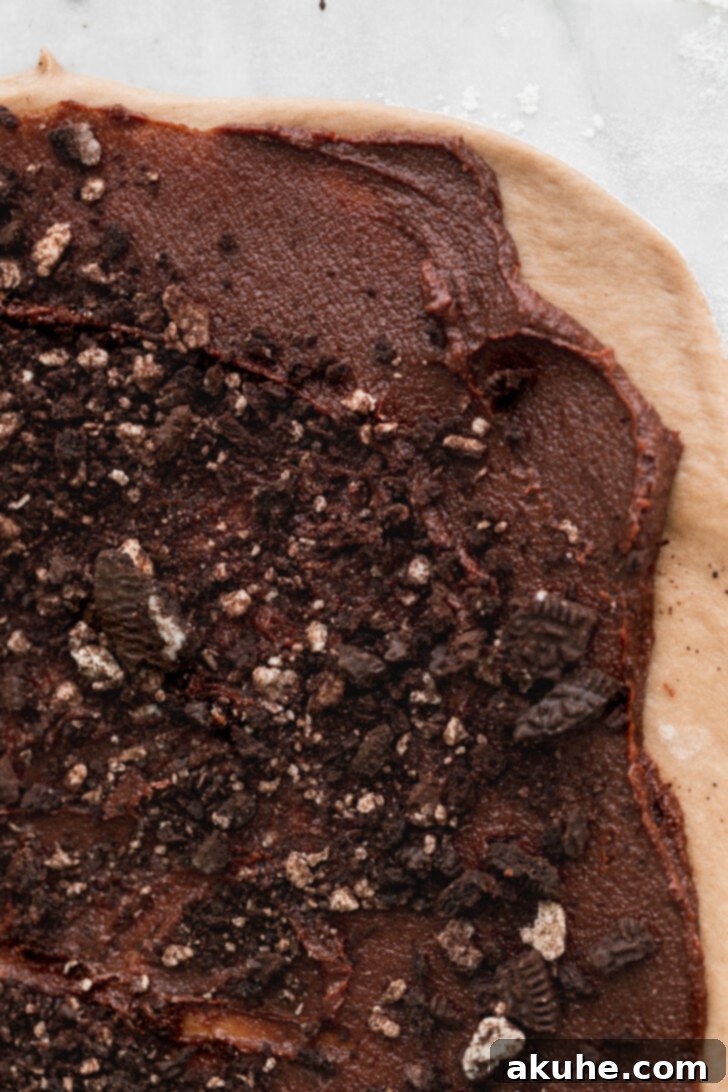 Rich chocolate cinnamon Oreo filling spread evenly over the rolled-out dough, with more Oreo pieces sprinkled on top.