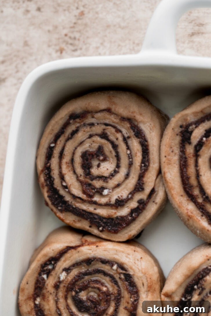 Unbaked cinnamon rolls arranged in a baking pan, with heavy cream poured around them for extra moisture.