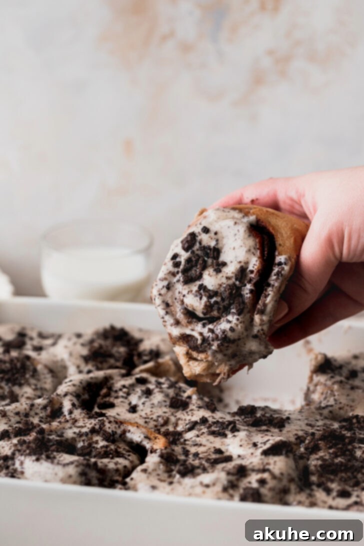 A hand reaching in to pull a single, warm Oreo cinnamon roll from the pan, showing its gooey texture.