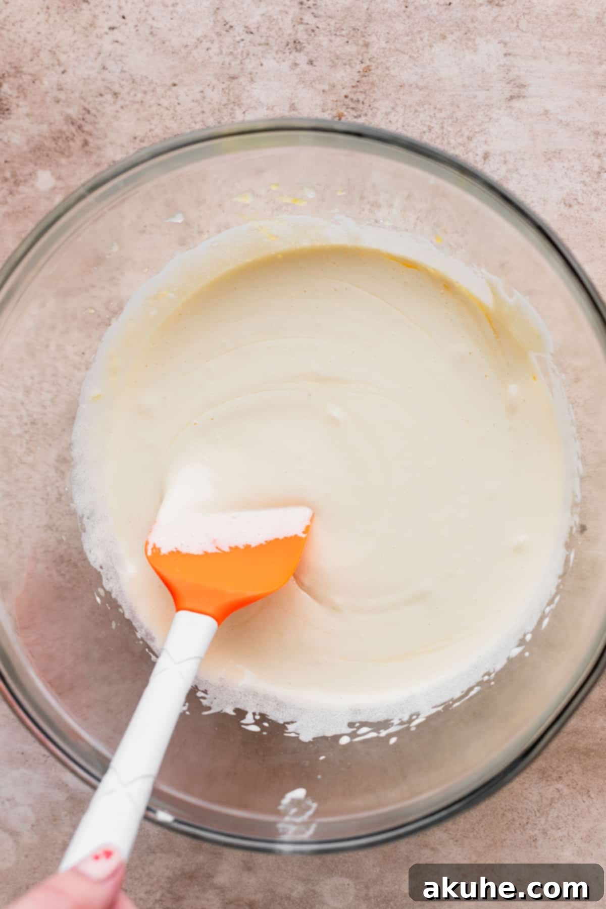 Artisan Brownie Bites 4 Whipped sugar and eggs in a glass bowl with a rubber spatula, showing the light and airy texture.