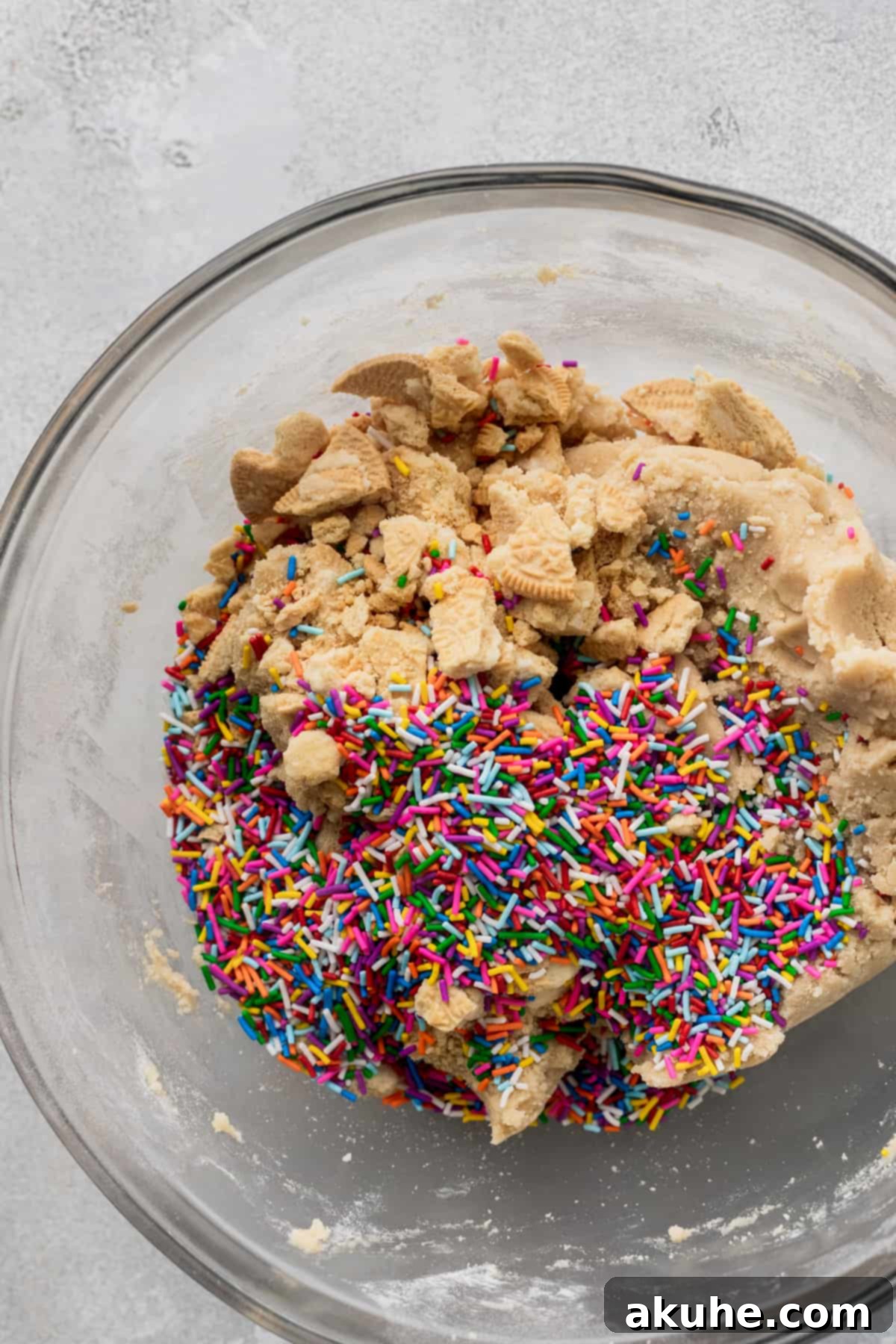 Celebratory Cookie Confections 5 The vibrant addition of rainbow sprinkles and golden Oreo chunks being mixed into the rich cookie dough in a glass bowl.