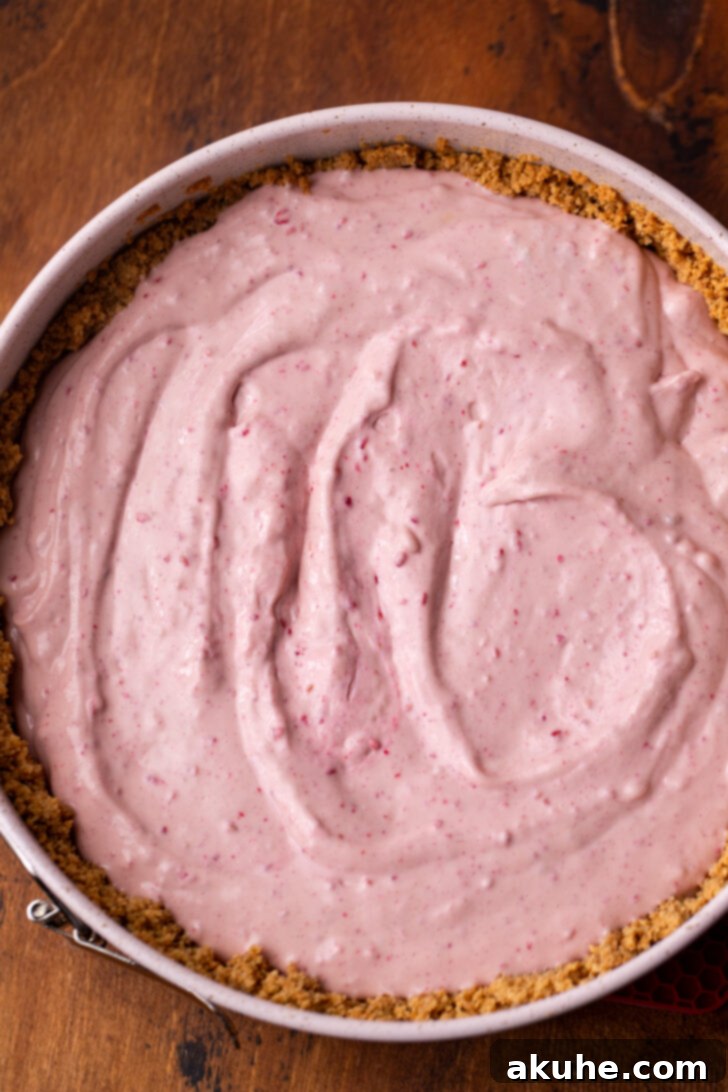 The cheesecake batter being poured into a pre-baked graham cracker crust, ready for baking.