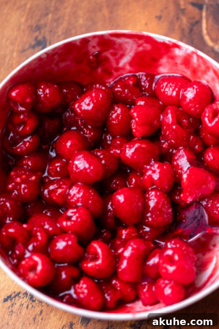 A bowl of homemade raspberry sauce, thick and glossy, with fresh raspberries ready to be added.