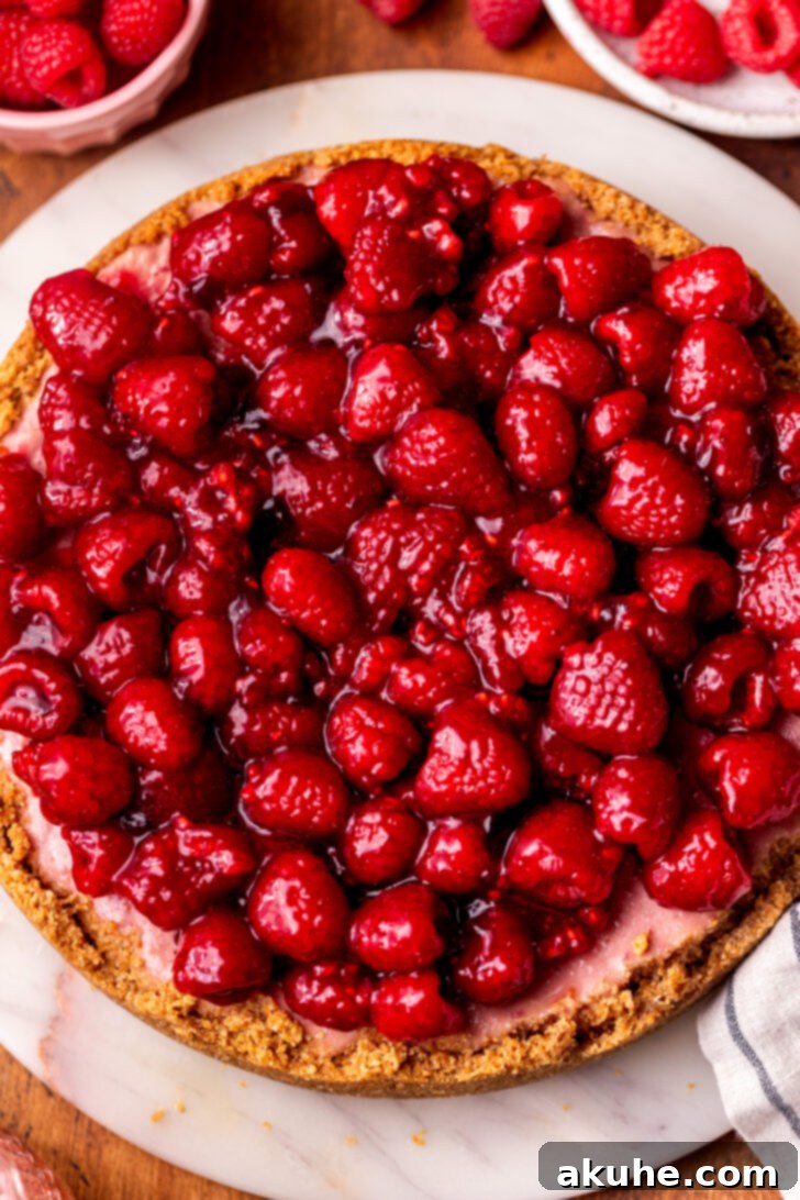 A beautifully decorated raspberry cheesecake, with fresh raspberries arranged artfully on top of the glossy raspberry sauce.