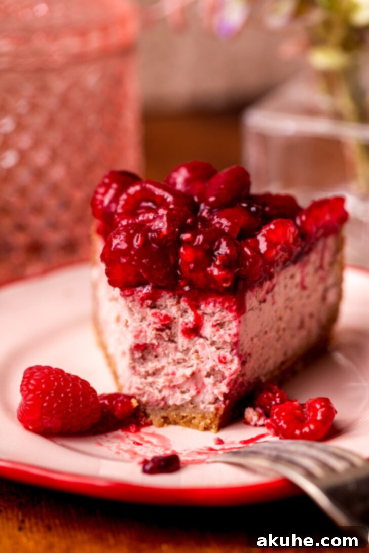 A single slice of raspberry cheesecake on a plate, with a bite missing, inviting you to indulge in its deliciousness.