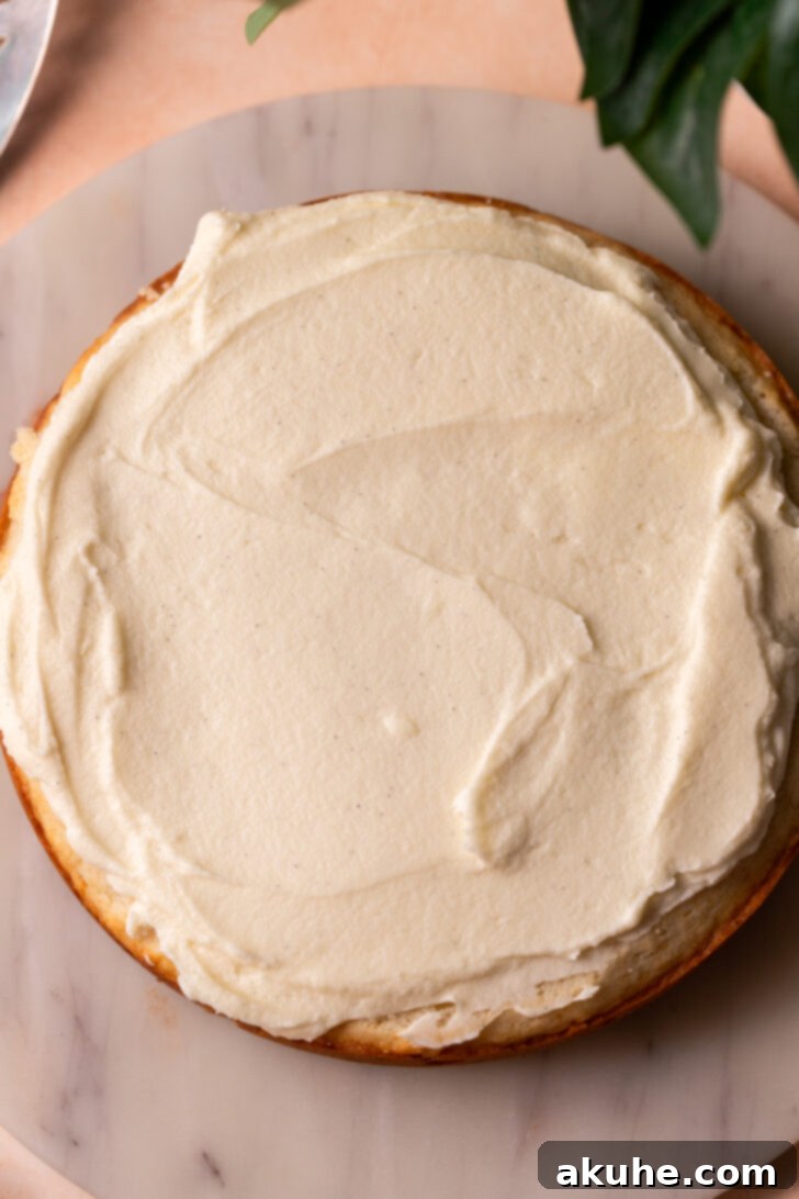 The Ultimate Vanilla Cake Experience 6 Spreading a generous layer of frosting on top of a cake layer.